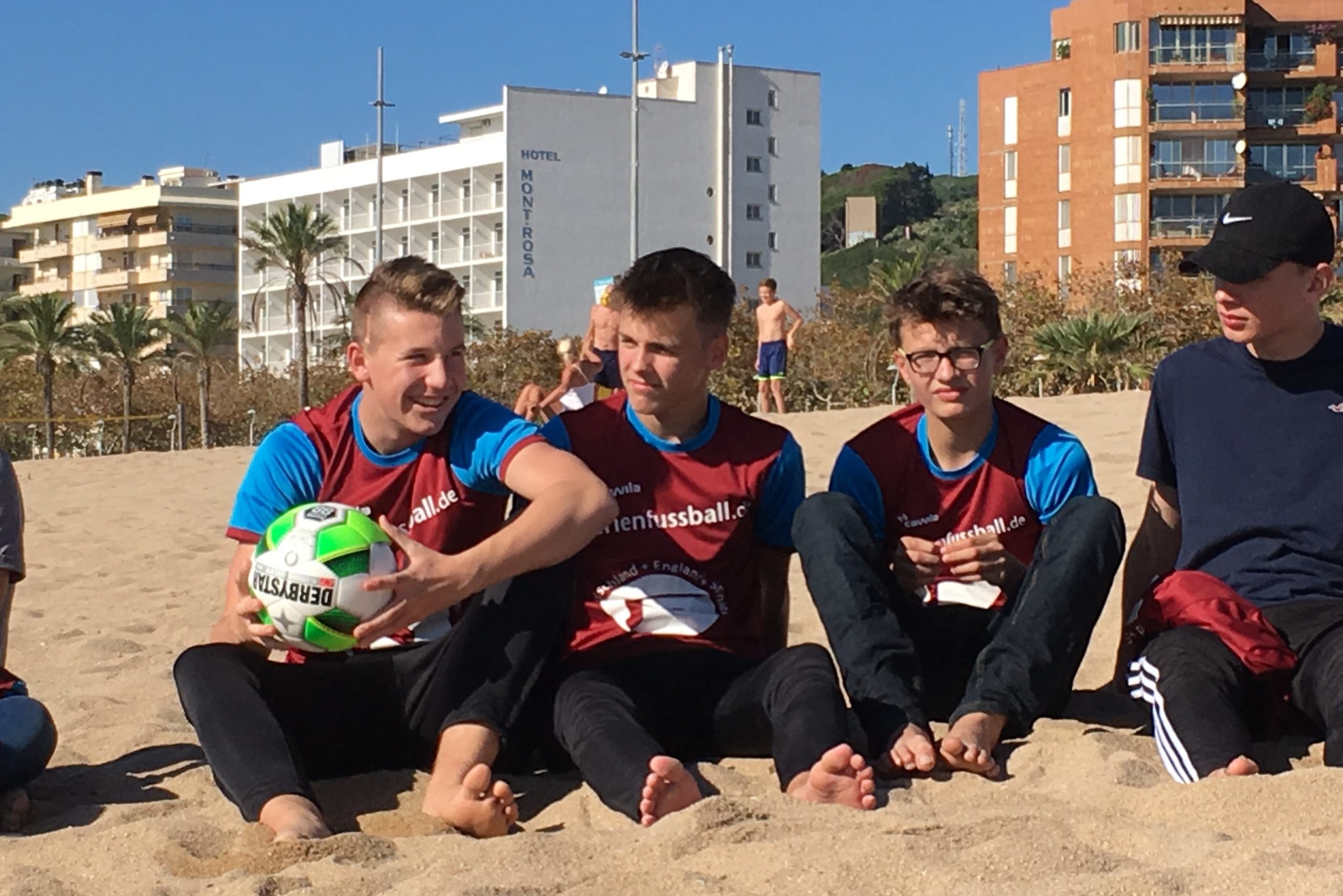 Jungen sitzen mit Ball am Strand