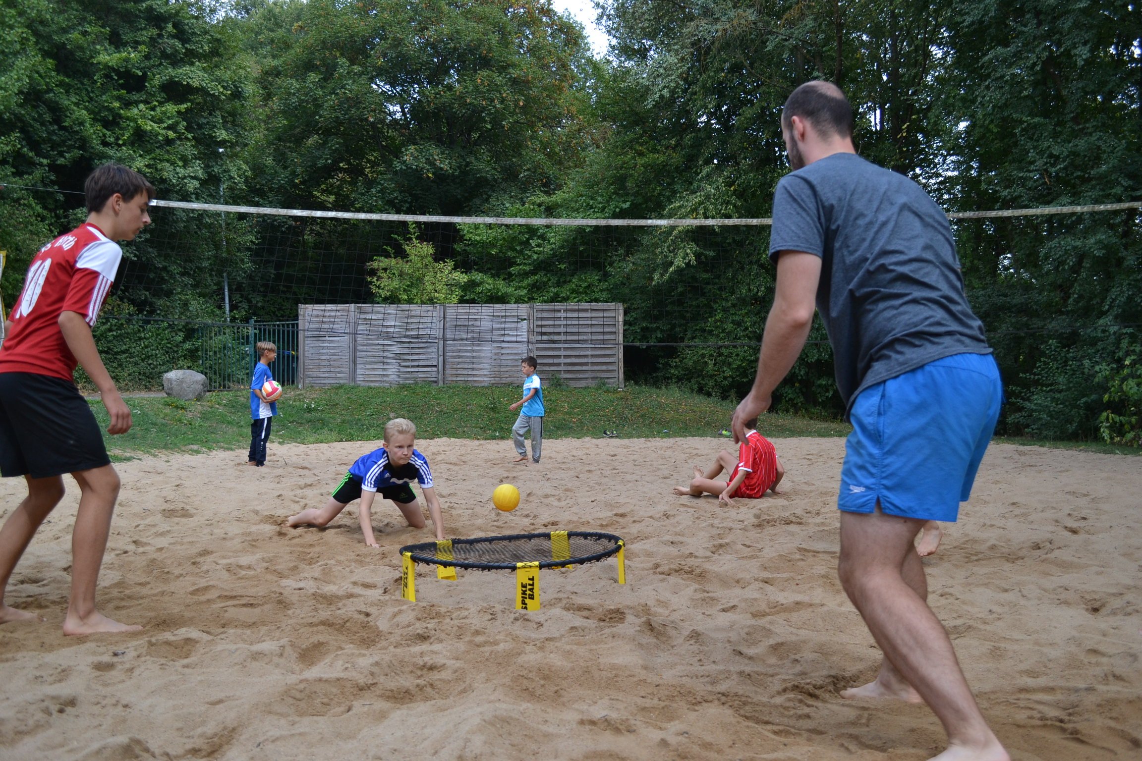 Jugendliche und ein Erwachsener beim Spikeball-Spielen im Sand.