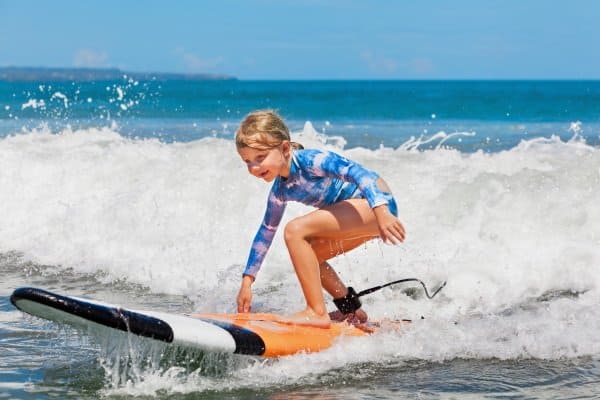 Mädchen steht auf Surfbrett und surft im Meer eine Welle