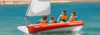 Vier Kinder mit Schwimmwesten auf einem Segelboot im Meer