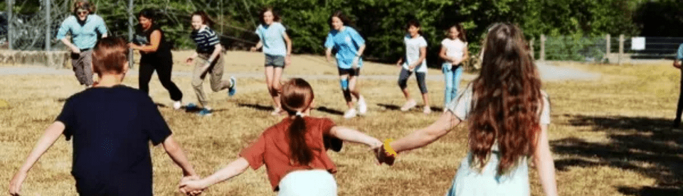 Kinder halten sich an den Händen, spielen draußen auf der Wiese