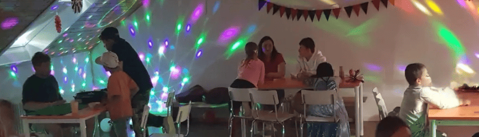 Kinder an Tischen in einem Raum mit Partybeleuchtung