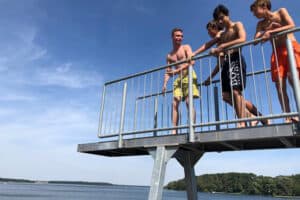 Kinder springen von einem Sprungturm in einen See