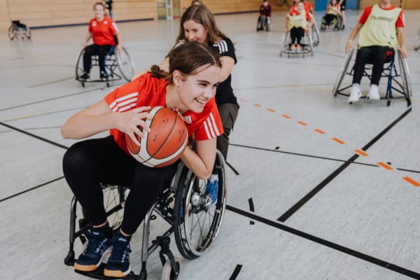 Mädchen wird im Rollstuhl geschoben mit Basketball