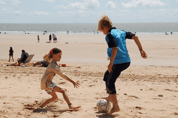Junge und Mädchen spielen Fußball am Strand